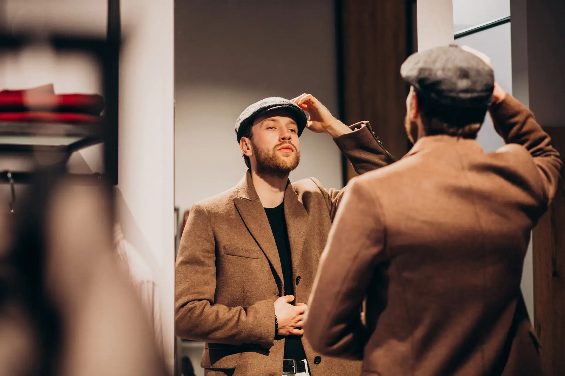 Homem utilizando um newsboy, um dos diversos tipos de chapéu masculino. Ele utiliza também uma camiseta preta sob um blazer bege.