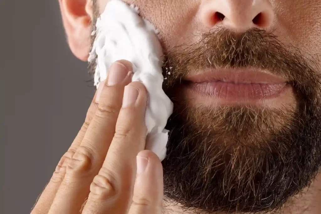 Homem aplicando espuma de barbear sobre a barba. Essa é uma etapa fundamental de como fazer a barba corretamente.