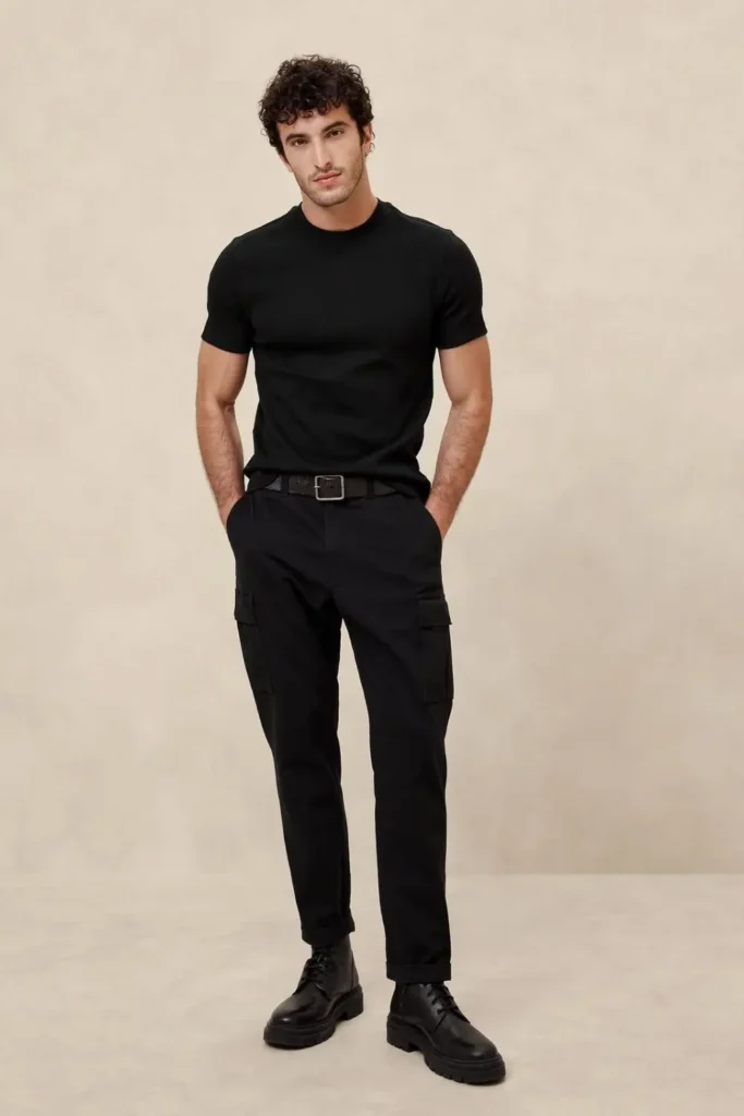 Homem usando um look all black masculino casual, com botas de couro, calça de sarja e camiseta básica.