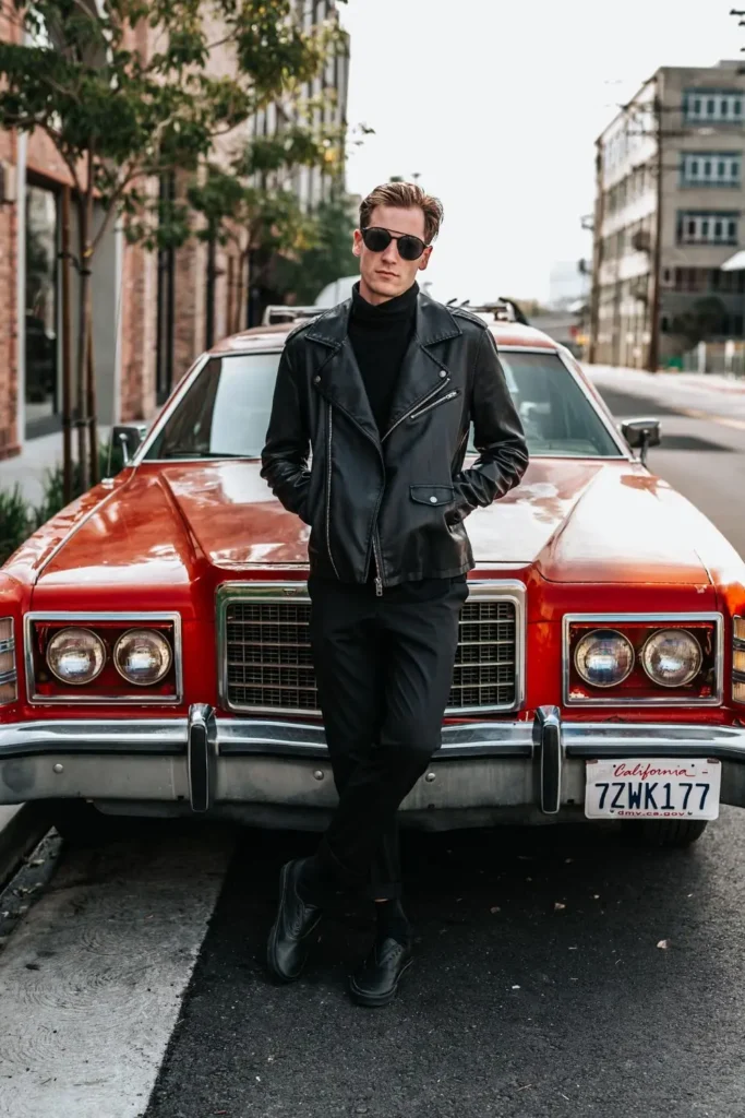 Homem usando um visual todo preto estilo rock, com tênis de couro, calça chino, camiseta gola alta e jaqueta de couro.