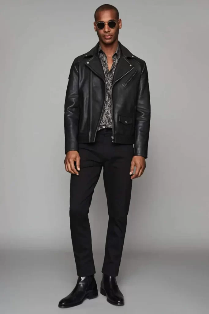 Homem usando um look all black masculino estilo rock, composto por: bota de couro, calça jeans, camisa e jaqueta de couro.