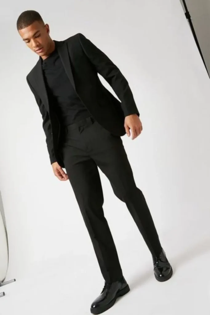 Homem utilizando um look all black smart casual, com bota de couro, calça de alfaiataria, camiseta e blazer.