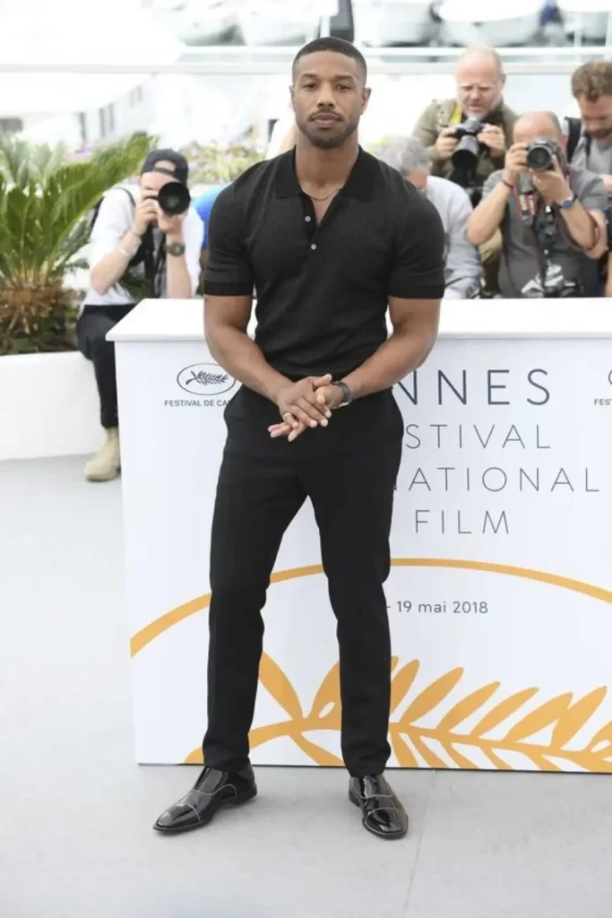 Ator Michael B Jordan usando um look masculino all black. Ele está de sapato social, calça e camisa polo.