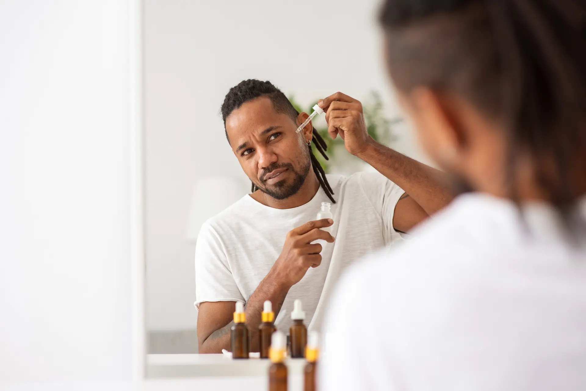 Homem realizando uma rotina de skincare masculino. Ele está diante de um espelho aplicando hidratante na pele do rosto.