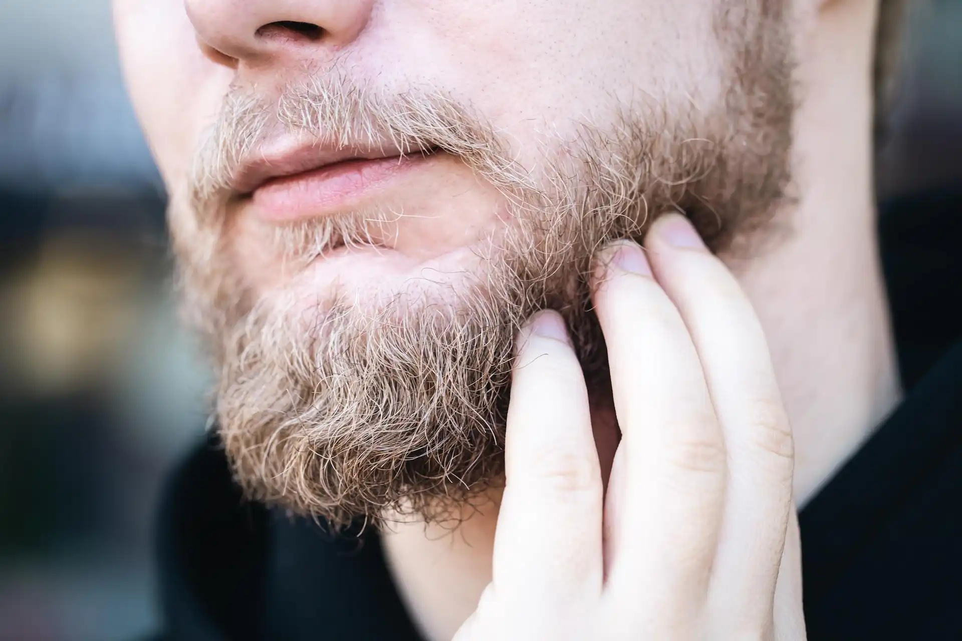 Zoom em um queixo barbudo com uma mão coçando a barba.