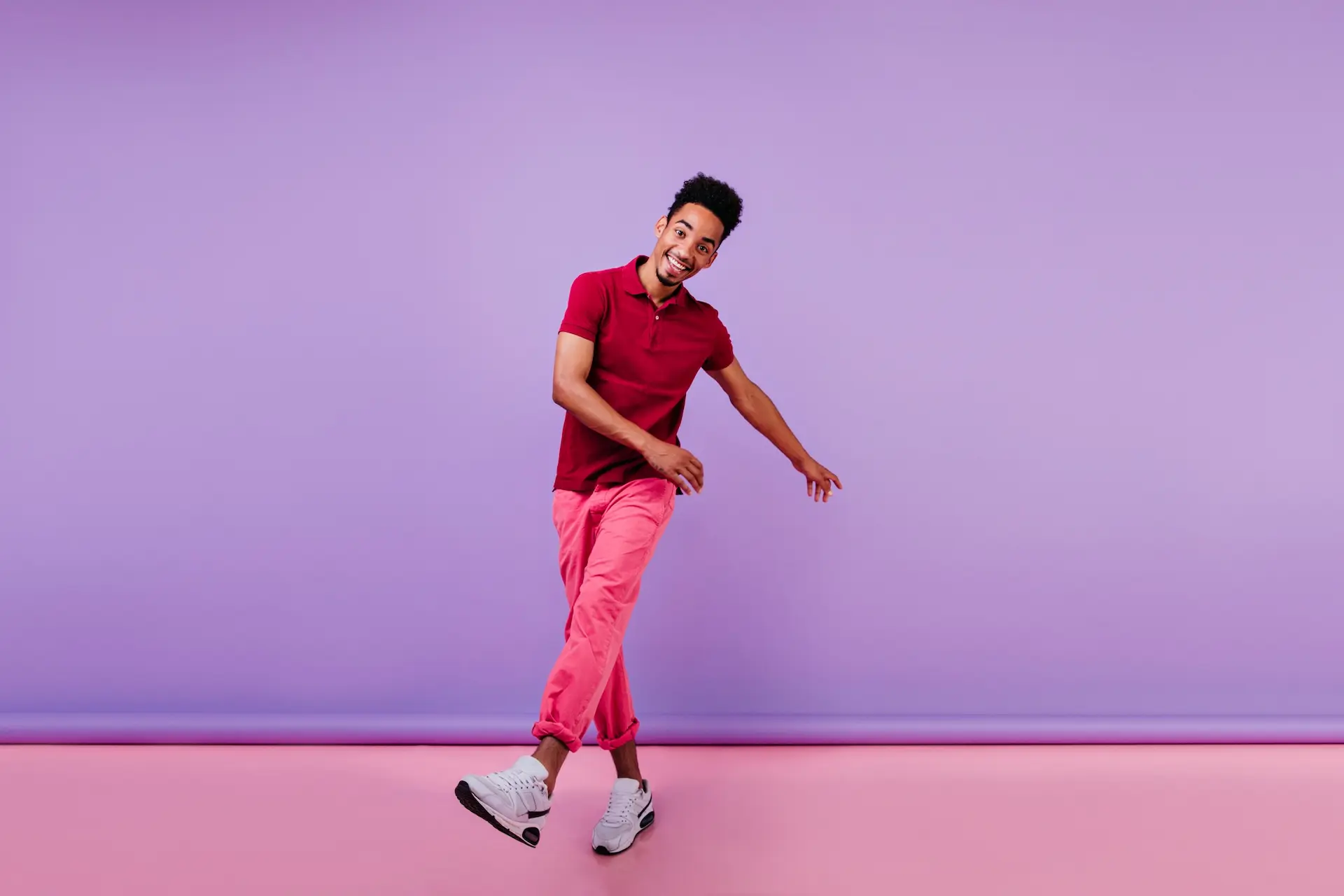 Homem usando camisa polo e calça em tons rosas, e tênis branco.