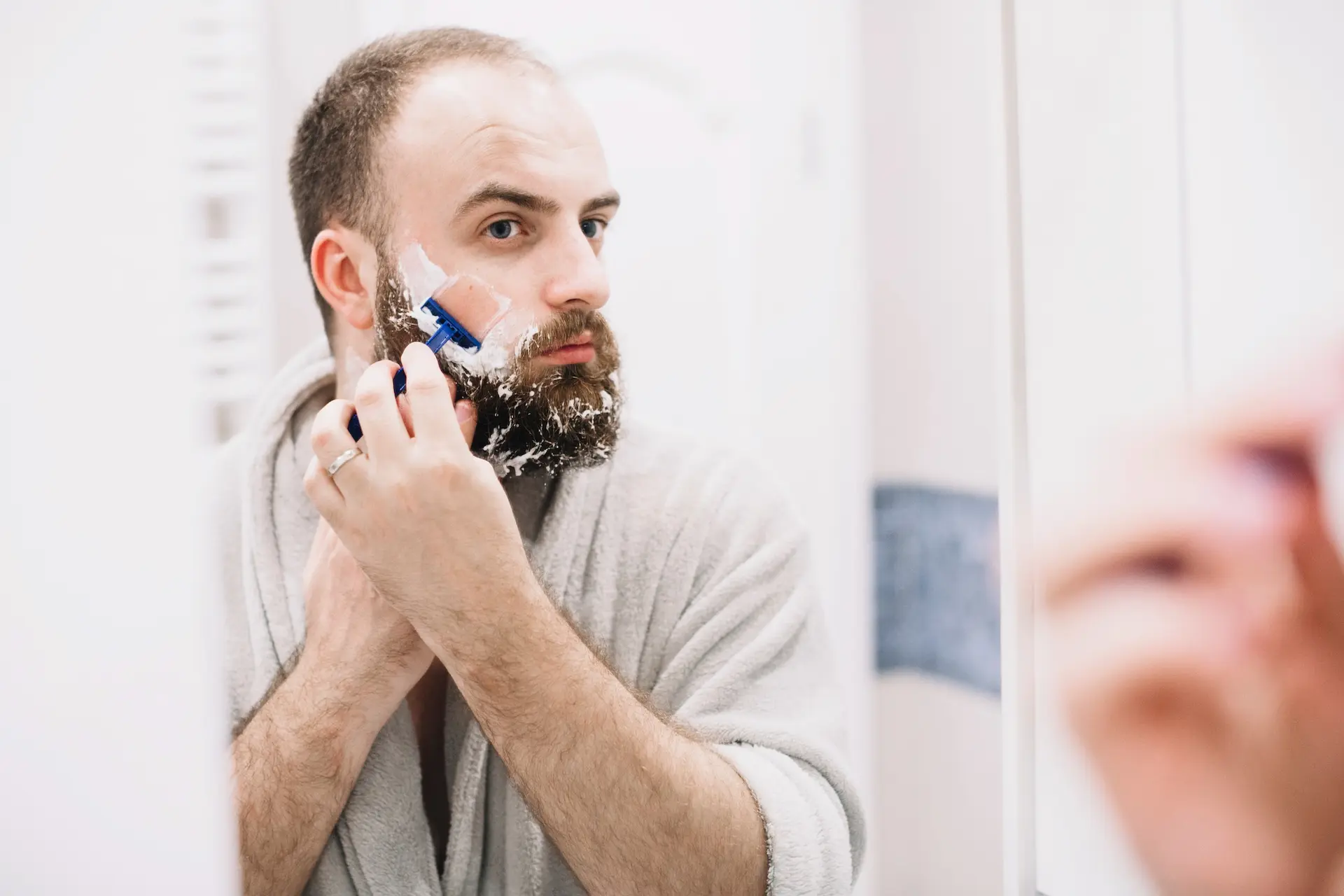 Homem fazendo a barba diante de um espelho.