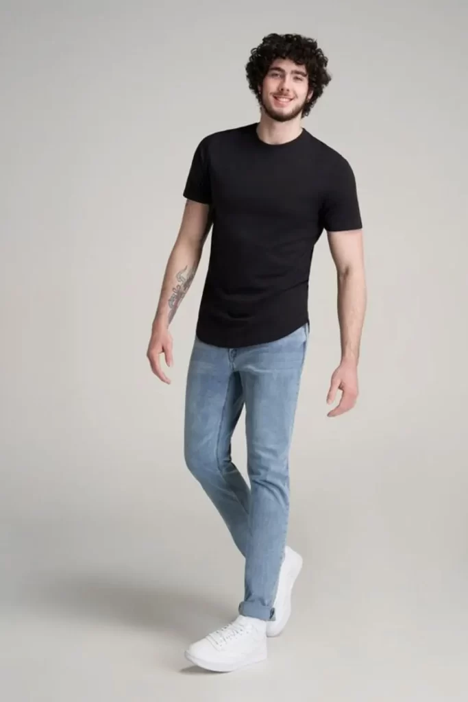 Homem usando calça jeans azul, camiseta básica preta e tênis casual branco. 