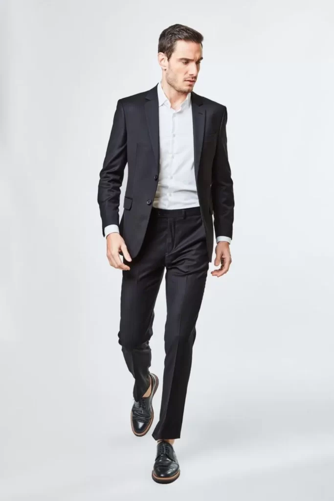 Homem usando calça chino, camisa e sapato social, e blazer. Exceto pela camisa branca, todas as peças são na cor preta. Esse é um dos looks masculinos para encontros mais indicados para momentos formais.