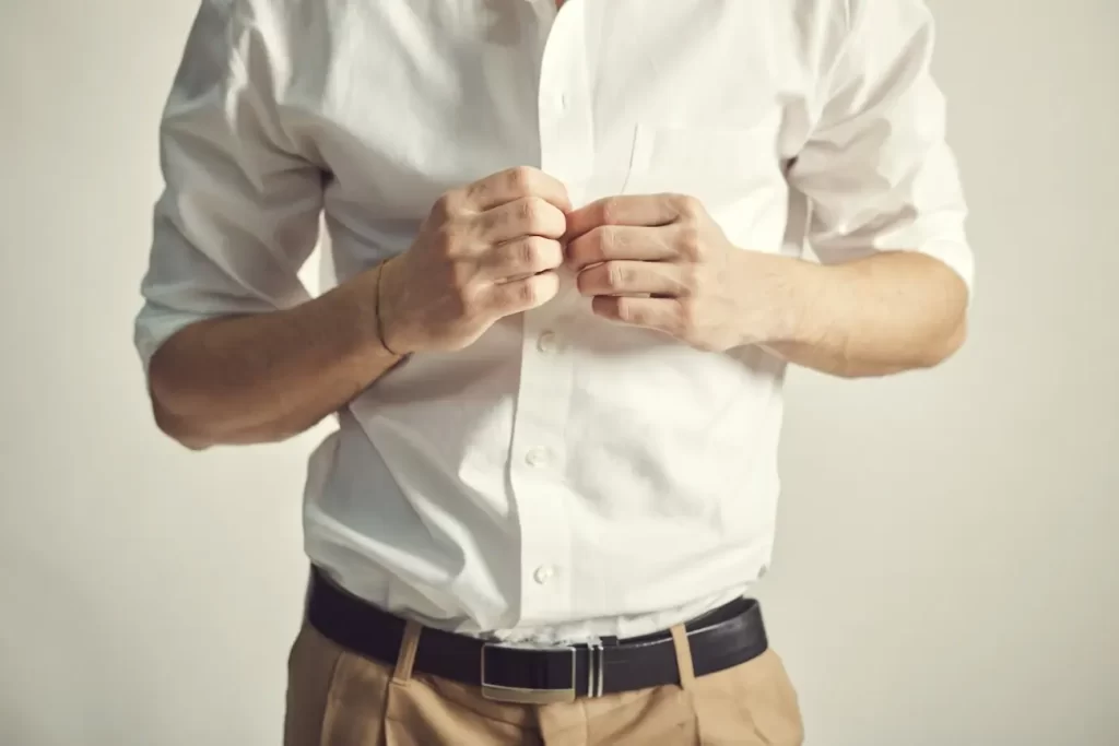 Homem abotoando uma camisa social branca.