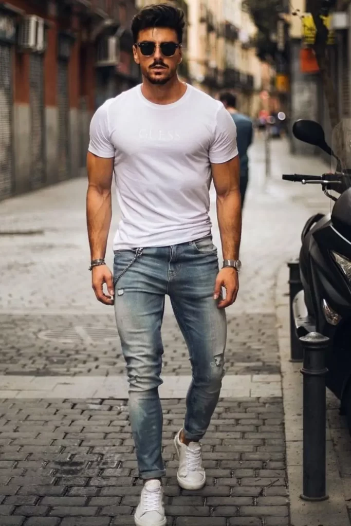 Homem usando camiseta branca, calça jeans azul, tênis branco e óculos de sol.