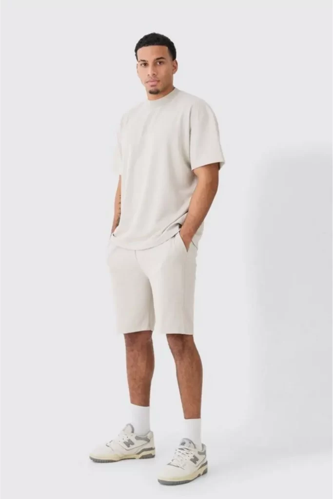 Homem usando bermuda, camiseta e tênis esportivo. Todas as peças apresentam um tom bege bem claro.