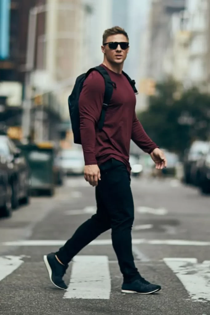 Homem usando camiseta de manga longa, calça e tênis esportivo. No rosto, óculos de sol. Além disso, ele carrega uma mochila preta nas costas.