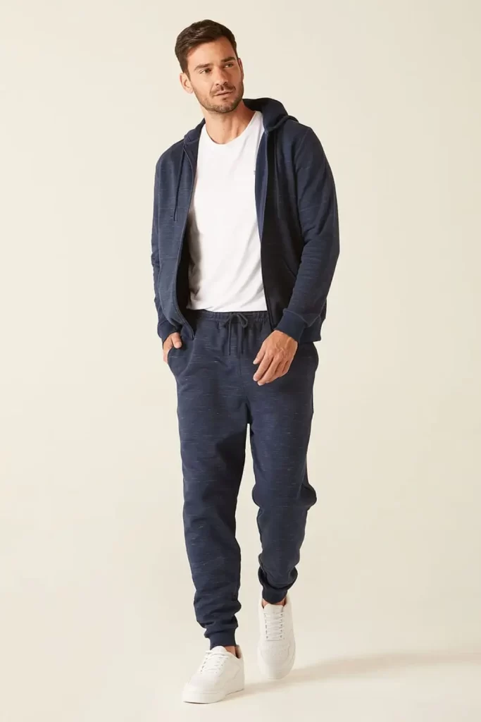 Homem usando calça jogger, camiseta, jaqueta e tênis esportivo.