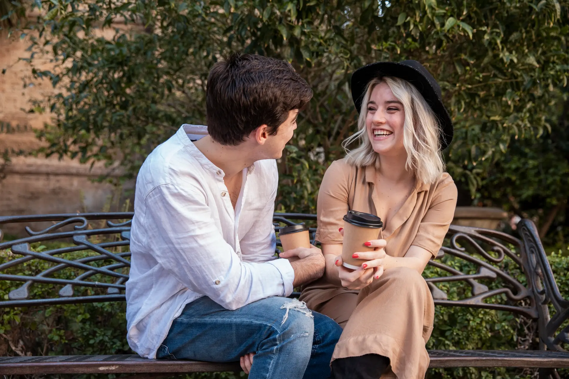 Ato de flertar entre um homem e uma mulher. Eles estão sentados em um banco de praça, se olhando e sorrindo.