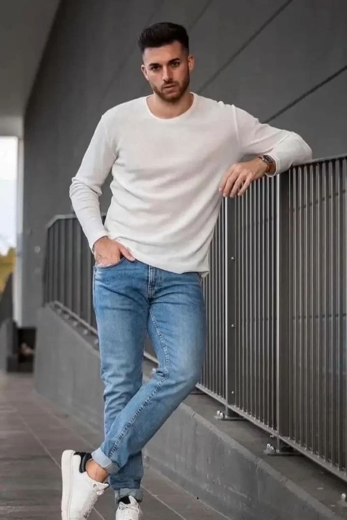 Homem usando calça jeans, camiseta branca de manga longa e tênis casual.