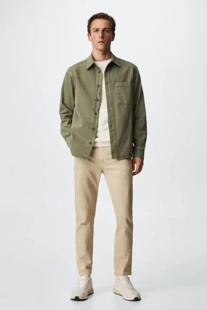 Homem usando calça chino bege, camiseta branca, jaqueta verde-oliva e tênis casual.