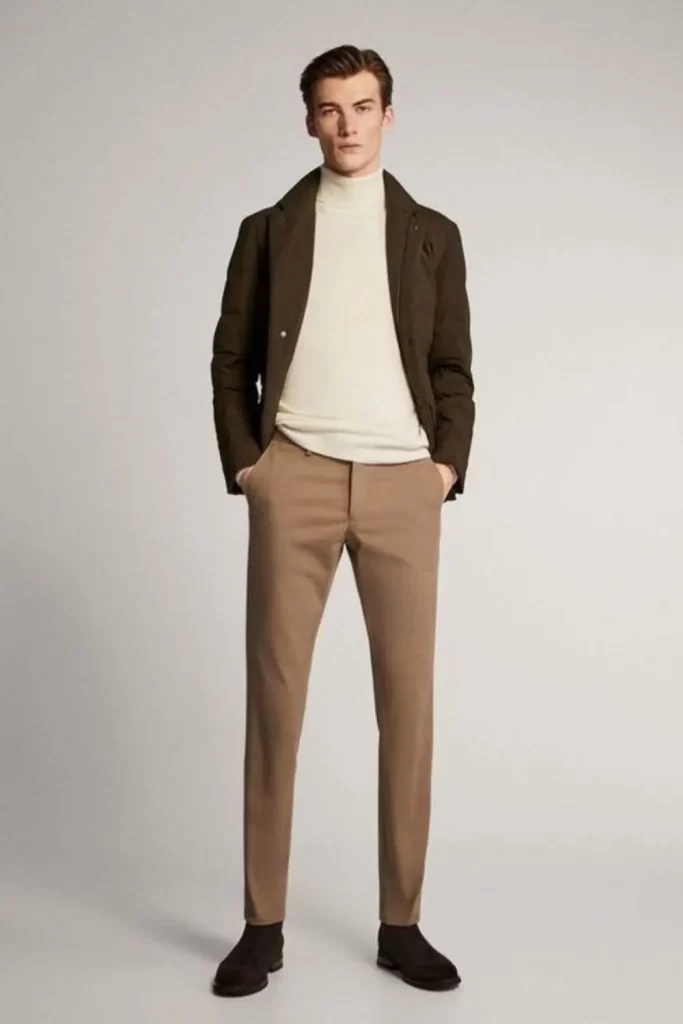 Homem usando calça de alfaiataria marrom-claro, camiseta gola alta creme, jaqueta marrom-escuro e botas.