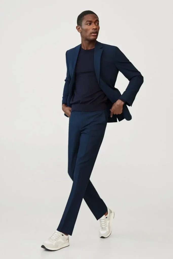 Homem usando tênis branco, calça de alfaiataria, camiseta básica e blazer.